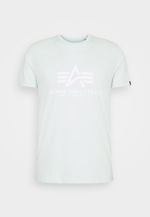 Svetlo mint zelena majica, kratki rukavi, okrugli izrez. Na prednji strani se nalazi beli logotip "Alpha Industries" sa geometrijskim dizajnom.