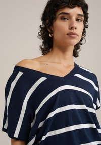 Marineblå och vit randig oversized stickad topp med avslappnad passform, korta ärmar och en v-ringning. Mjuk textur och horisontell mönstring.