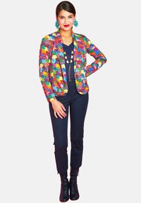 Colorful sequin blazer with floral patterns, paired with a dark top and pants. Black lace-up boots complete the outfit.