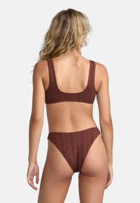 Brun bikini-set med texturerad tyg och blommönster. Toppen har breda band och en fyrkantig rygg, medan botten har en högskuren stil.