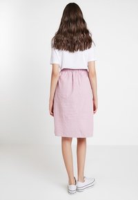 Jupe rose à rayures de longueur genou avec une taille élastique, associée à un t-shirt blanc et des baskets blanches. Texture lisse et coupe décontractée.