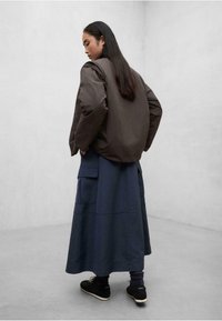 Chaqueta acolchada marrón con un diseño corto, combinada con una falda larga azul marino con bolsillos. Zapatillas negras completan el conjunto.