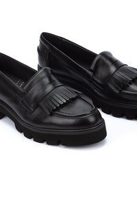 Mocasines de cuero negro con un detalle de flecos texturizado, punta redonda y suela gruesa de goma negra. Acabado limpio y suave en todo momento.