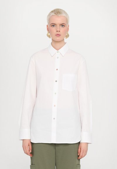 Camicia bianca con bottoni, maniche lunghe, caratterizzata da una singola tasca e bottoni multicolori lungo la parte anteriore. Tessuto liscia.
