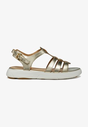 Sandale métallique dorée avec plusieurs bandes entrelacées, une bride ajustable à la cheville et une semelle blanche rembourrée. Texture lisse avec un minimum de pièces métalliques.