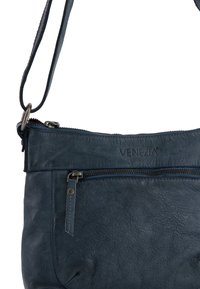 Modrá kožená crossbody taška s texturovaným povrchem, horním zipem a dodatečnou přední kapsou. Obsahuje ramenní popruh a logo.