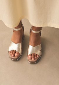 Fémes arany színű pántos szandálok széles keresztpánt dizájnnal, lapos talppal és bokapánttal; texturált anyag sima felületekkel.