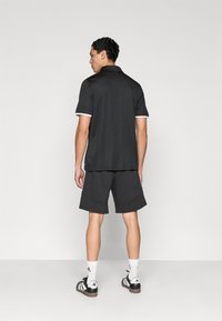 Μαύρο πόλο μπλουζάκι με λευκό περίγραμμα, συνδυασμένο με σκούρες βερμούδες. Λείο ύφασμα και άνετη εφαρμογή. Υποδήματα περιλαμβάνουν μαύρα και λευκά αθλητικά παπούτσια.