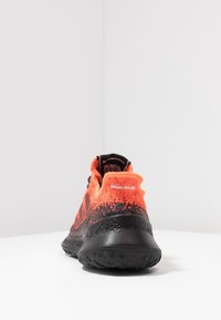 Černo-oranžová sportovní bota s texturovaným pleteným svrškem, polstrovaným límcem a pružnou gumovou podrážkou s přechodovým vzorem.