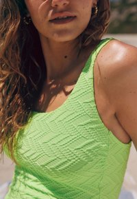 Maillot de bain texturé vert avec un motif géométrique, doté de larges bretelles et d'une finition lisse qui met en valeur sa coupe ajustée.