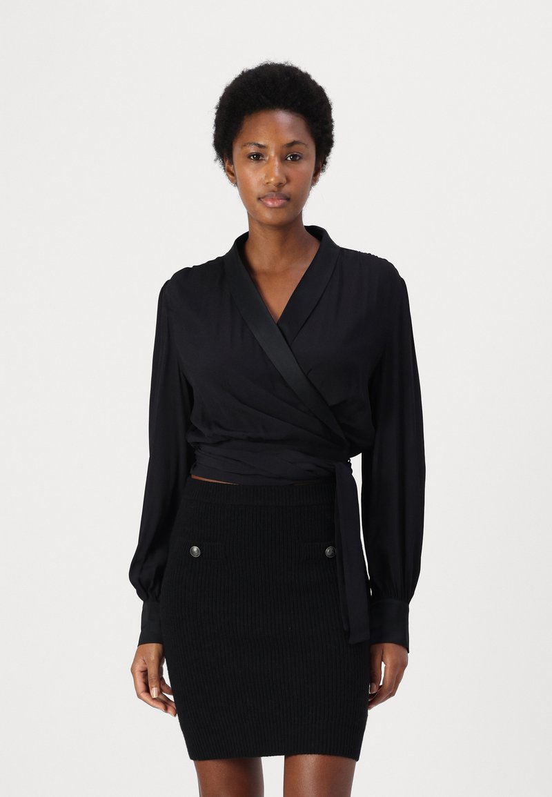 Blusa nera avvolgente con maniche lunghe e dettagli in satin, abbinata a una gonna aderente a coste nera con bottoni sulla parte anteriore.