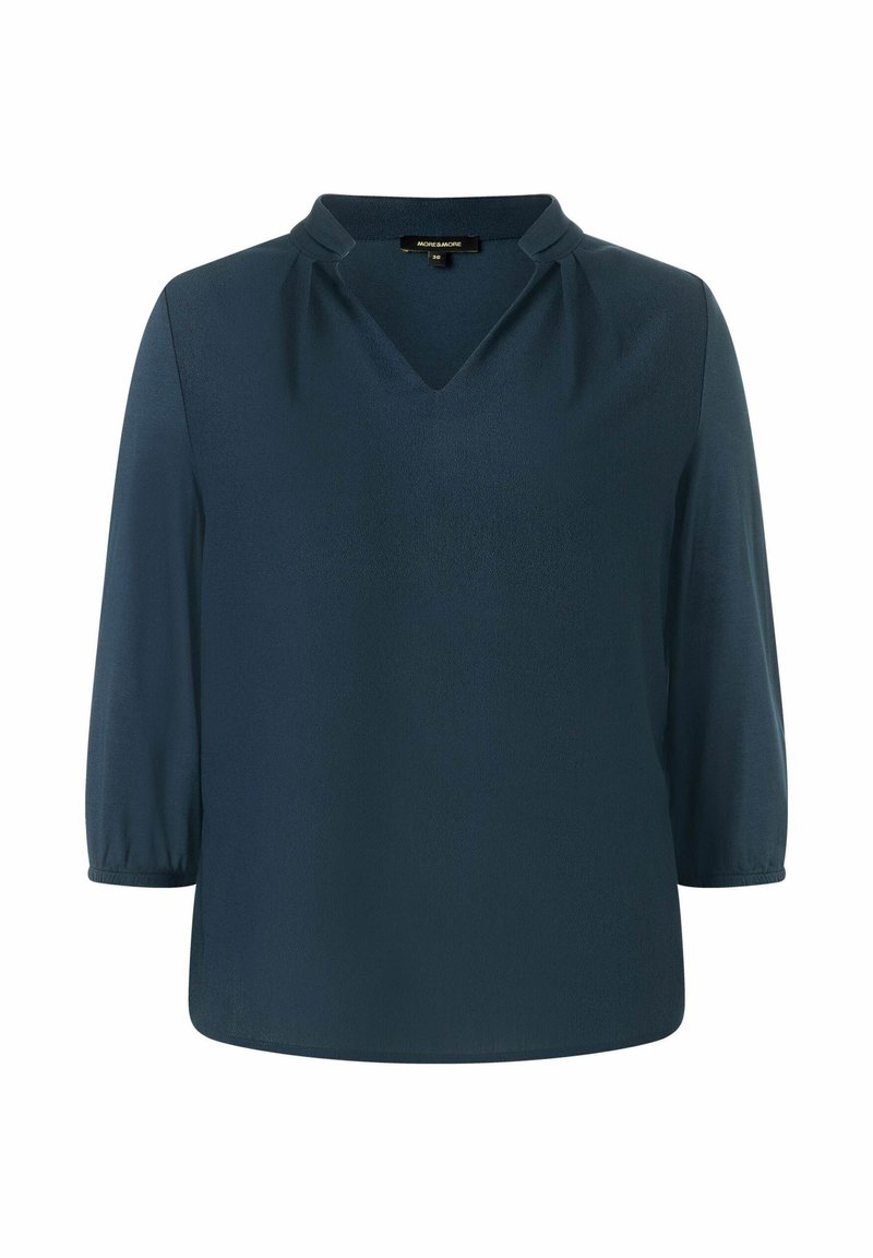 Blouse bleu marine en tissu lisse, avec un col en V, de légers plissés aux épaules et des manches trois-quarts.