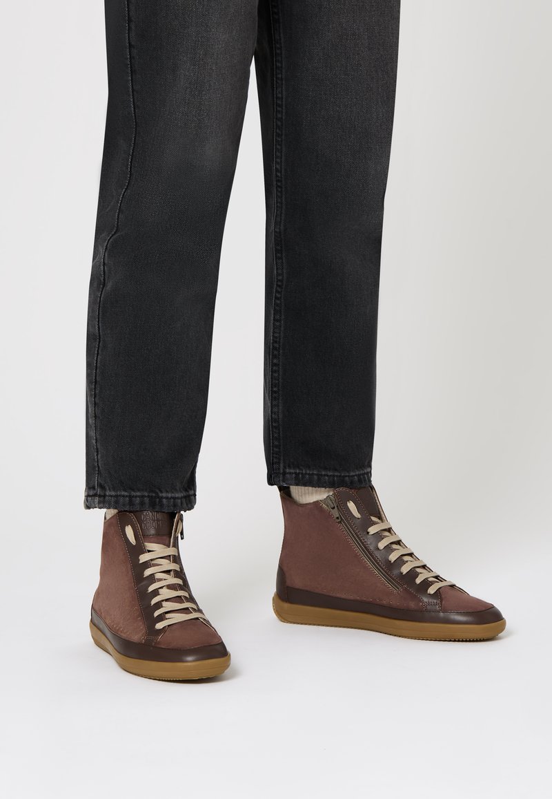 Sneaker alte marroni con lacci beige, materiali in tessuto e pelle, suola in gomma, zip laterale e dettagli a contrasto marroni.