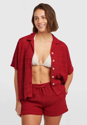 Camiseta roja de punto de manga corta con cierre de botones, combinada con pantalones cortos de punto a juego. Ambas piezas presentan un patrón texturizado y un ajuste casual.