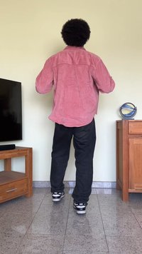 Rød cordfløyelskjorte, bakvinkel, brukt over svarte jeans og svarte joggeskinn. Jevn tekstur, avslappet passform, lange ermer og fremtredende sømmer.