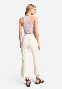 Gestreiftes, ärmelloses Tanktop kombiniert mit hochtaillierten, weit geschnittenen weißen Hosen; das Model trägt zudem braune Riemchensandalen.