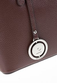 Borsa a tracolla in pelle marrone effetto texturizzato con accento circolare in metallo argentato, dotata di una sottile tracolla e dettagli di cucitura ben visibili.