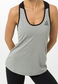 Jasnoszary sportowy top na ramiączkach z czarnymi paskami, z dekoltem w serek i logo Reebok, wykonany z gładkiego, oddychającego materiału.