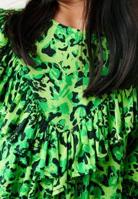 Haut vert à volants avec un imprimé animal noir et vert audacieux. Fabriqué en tissu léger avec un col rond et des détails texturés.