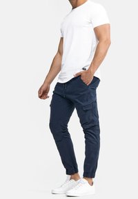 Witte t-shirt met korte mouwen, gecombineerd met marineblauwe joggingsbroeken met zijzakken en elastische boorden, aangevuld met witte sneakers.