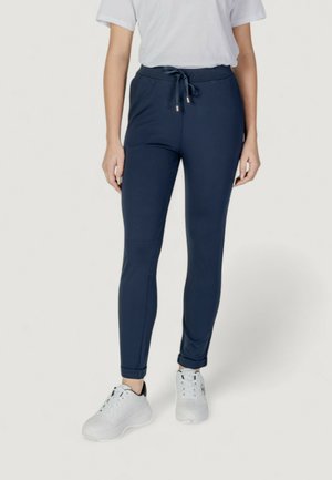 Pantaloni jogger blu navy realizzati in tessuto elasticizzato, con vita regolabile tramite cordoncino, gambe affusolate e polsini alla caviglia, abbinati a sneaker bianche.