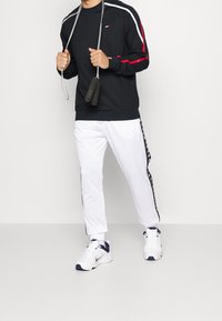 Felpa nera con strisce laterali rosse e bianche, abbinata a pantaloni da allenamento bianchi con una striscia laterale nera a motivo. Sono presenti accessori per il fitness.