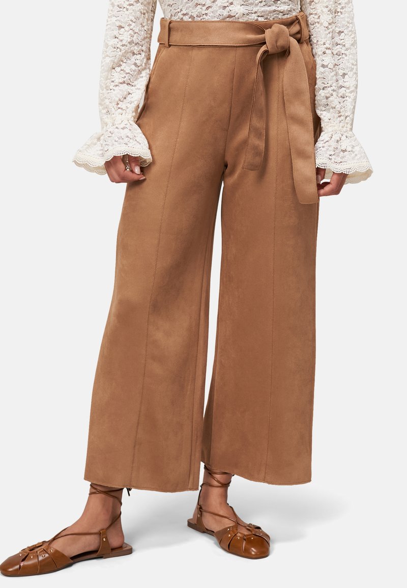 Pantalons à jambes larges en daim marron avec une ceinture à nouer, dotés de poches latérales et d'une texture lisse. Associés à des chaussures plates à brides marron.