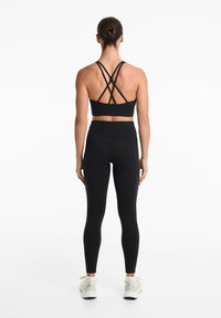 Svart sportbh med korsade axelband, i kombination med högmidjade svarta leggings. Slät tyg och åtsittande design med vita sneakers.