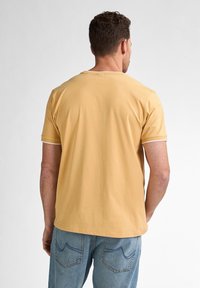 Tricou galben cu mânecă scurtă, de tip crew neckline, cu margine albă la mâneci, asortat cu blugi albaștri care au cusături la buzunarele din spate.