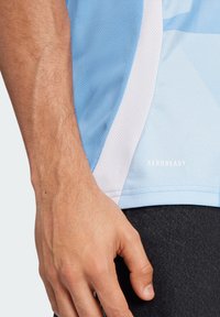Camisa deportiva de color azul claro, hecha de una tela transpirable, con una superficie texturizada, detalles en blanco y el logo "AEROREADY" cerca del dobladillo.