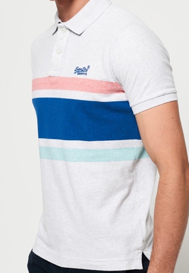 Homme portant un polo blanc avec des rayures horizontales rose, bleue, blanche et bleu clair sur la poitrine.