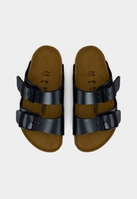 Μαύρα δερμάτινα σανδάλια με δύο ρυθμιζόμενες αγκράφες και καφέ σουέντ πάτους, σε θέα από πάνω σε λευκό φόντο.