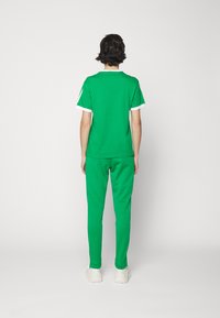 Green cotton t-shirt and matching sweatpants with white accents, featuring a relaxed fit and smooth texture, worn with white sneakers.