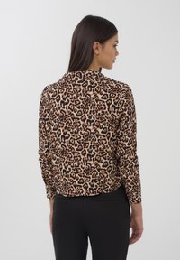 Blusa in stampa leopardata realizzata in tessuto leggero, con maniche lunghe e colletto classico. Il motivo è composto da macchie marroni e nere su uno sfondo beige.