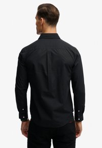 Camicia nera a maniche lunghe con polsini con bottoni, vestibilità sagomata, dettaglio con piega sul retro, tessuto liscio e etichetta con marchio discreta all'orlo.