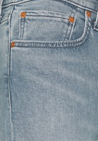 Jeans de denim azul claro con un diseño de cinco bolsillos, herrajes en tono cobre y detalles de costura visibles. Textura suave con un ligero desvanecimiento.