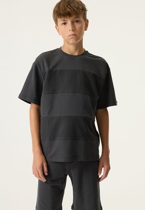 Camiseta negra de manga corta con franjas horizontales texturizadas, cuello redondo acanalado y ajuste holgado. Combinada con pantalones cortos oscuros a juego.