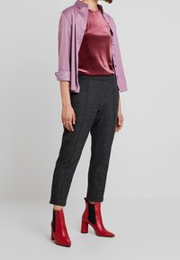 Ljuslila skjorta med knappar, lagd över en vinröd sammetsöverdel, kombinerad med skräddarsydda svarta byxor och röda ankelstövlar med blockklack.