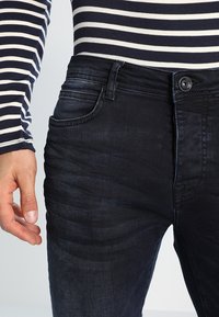 Jeans in denim blu scuro con vestibilità slim, caratterizzati da un classico design a cinque tasche e chiusura anteriore con bottone. Il tessuto ha una texture morbida.