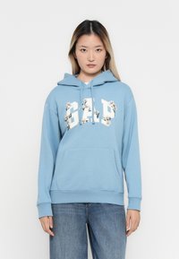 Light blue hoodie made of soft fabric, featuring a front pocket and a floral-embellished "GAP" logo on the chest.