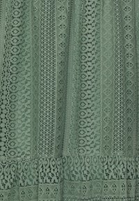 Tissu en dentelle verte avec des rayures verticales présentant des motifs floraux et géométriques, et un ourlet festonné en bas.
