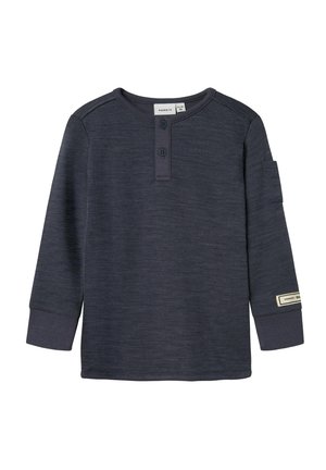 Camisa de niño de manga larga en gris oscuro con cuello redondo, tapeta de botones con dos botones, y un pequeño parche en el puño de la manga izquierda.