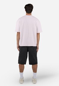 Light pink ribbed short-sleeve t-shirt worn with black denim shorts, featuring a relaxed fit and straight hem. White socks and sneakers are visible.