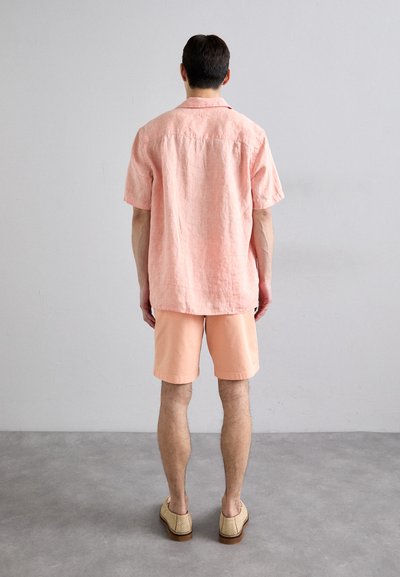 Camicia leggera a maniche corte e pantaloni corti abbinati in tessuto rosa pastello, abbinati a scarpe intrecciate. Design semplice e dalle linee rilassate.