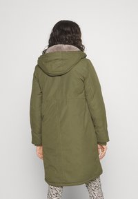 Abrigo parka largo de color oliva con capucha, que presenta un forro beige suave, cintura entallada y corte recto, hecho de un tejido texturizado.