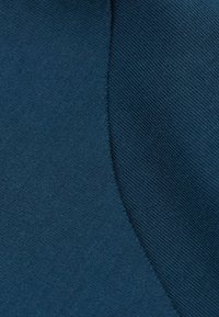 Teal tyg med en slät textur, med en diagonal söm som skapar en subtil kontrast mellan två sektioner.