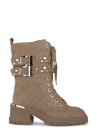 Stivale alla caviglia in suede trapuntato color ocra con fibbie metalliche, borchie e un tacco spesso. Presenta una chiusura con lacci e una suola testurizzata.