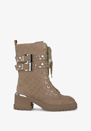 Bruine, gewatteerde suède enkelboot met metalen gespen, studs en een chunky hak. Voorzien van een vetersluiting aan de voorkant en een gestructureerde zool.