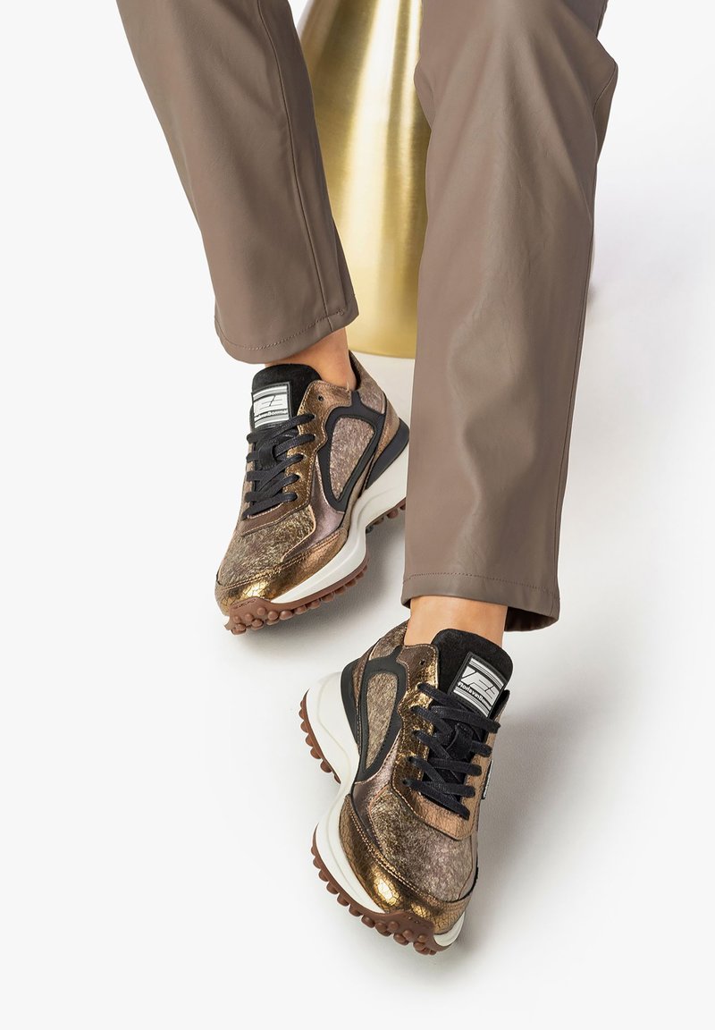 Sneaker marroni e neri con accenti dorati metallici, superficie testurizzata e suola chunky; design con lacci e dettaglio del logo sulla linguetta.