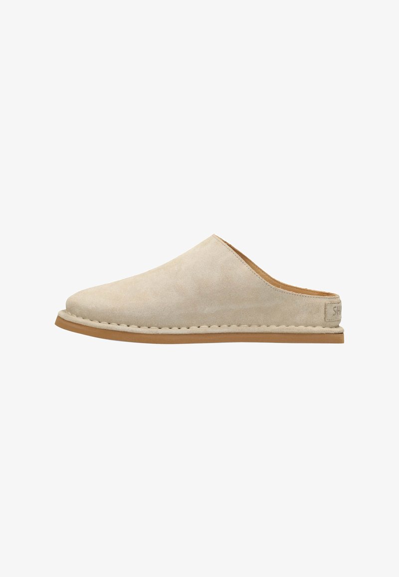 Chaussure beige en daim à enfiler avec une texture lisse, bout arrondi et semelle en caoutchouc cousue. Design minimaliste avec une étiquette logo à l'arrière.
